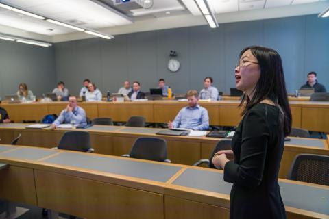Professor addressing a lecture hall of professionally-dressed students