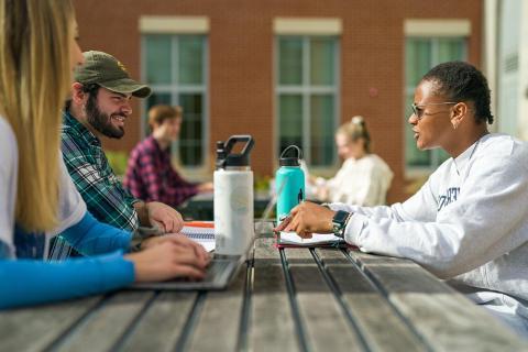 Students sitting outdoors on campus chatting at a picnic table