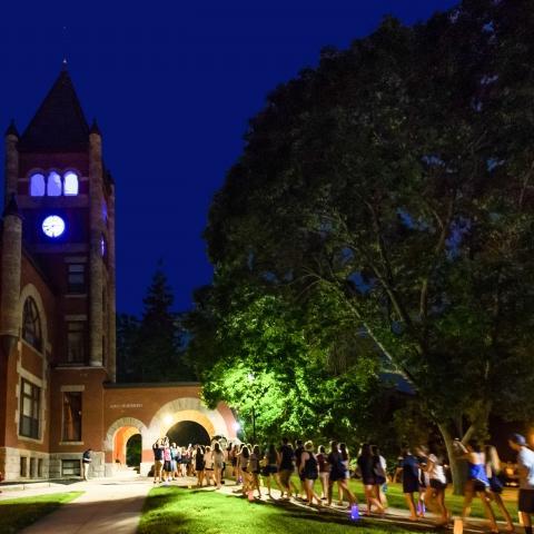 students walking under arch of Thompson Hall at night