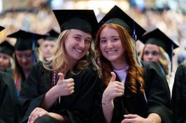 Two female students give the thumbs up at commencement